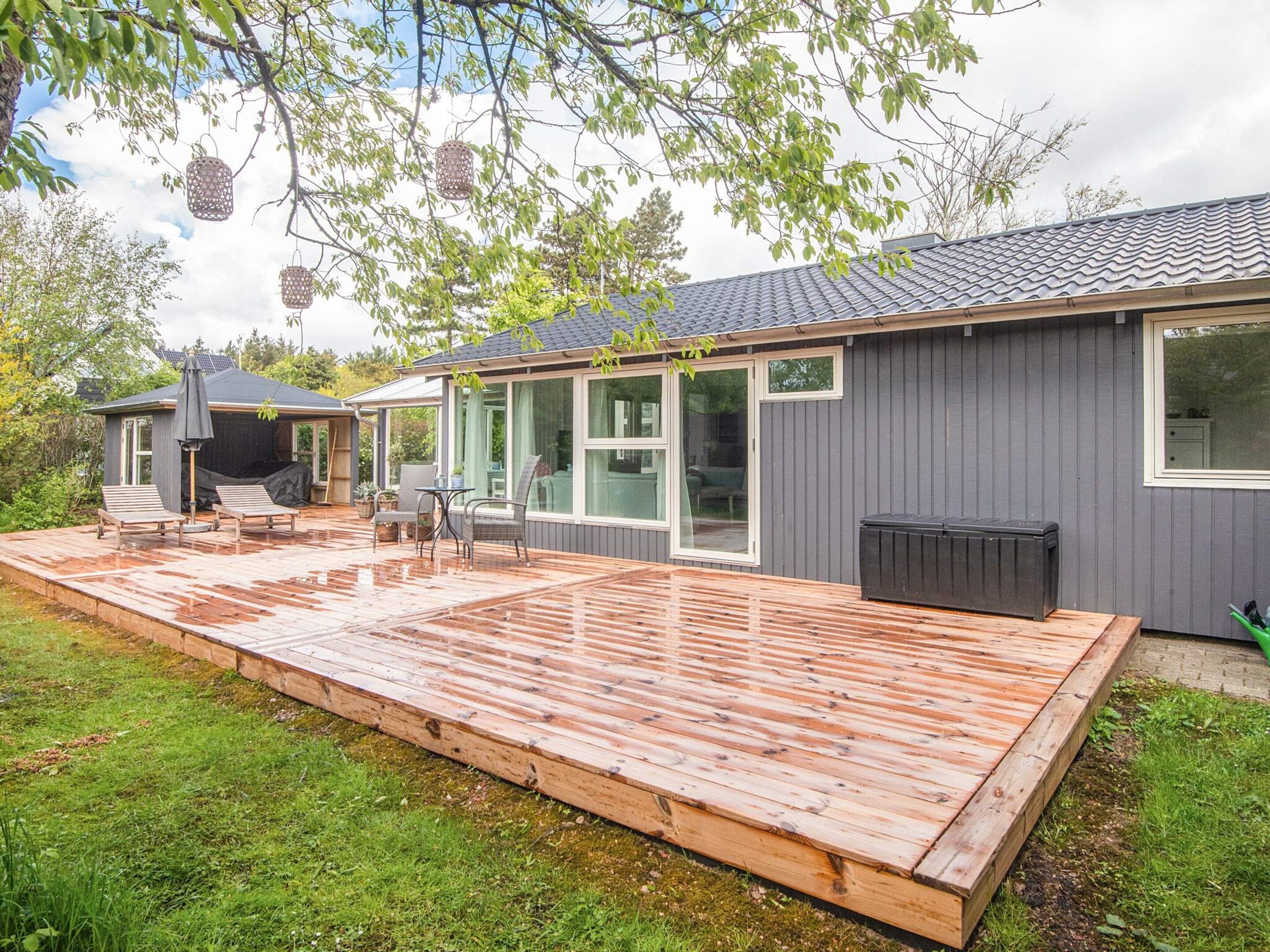 Ein modernes Haus mit Holzterrasse, großen Fenstern und einer überdachten Sitzgruppe im Freien.