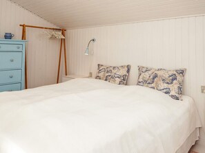 A bedroom with a bed, a dresser, a hanging rack, and a wall-mounted lamp.