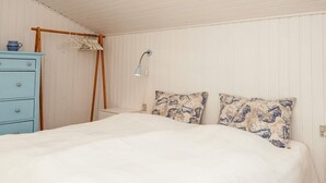 A bedroom with a bed, a dresser, a hanging rack, and a wall-mounted lamp.