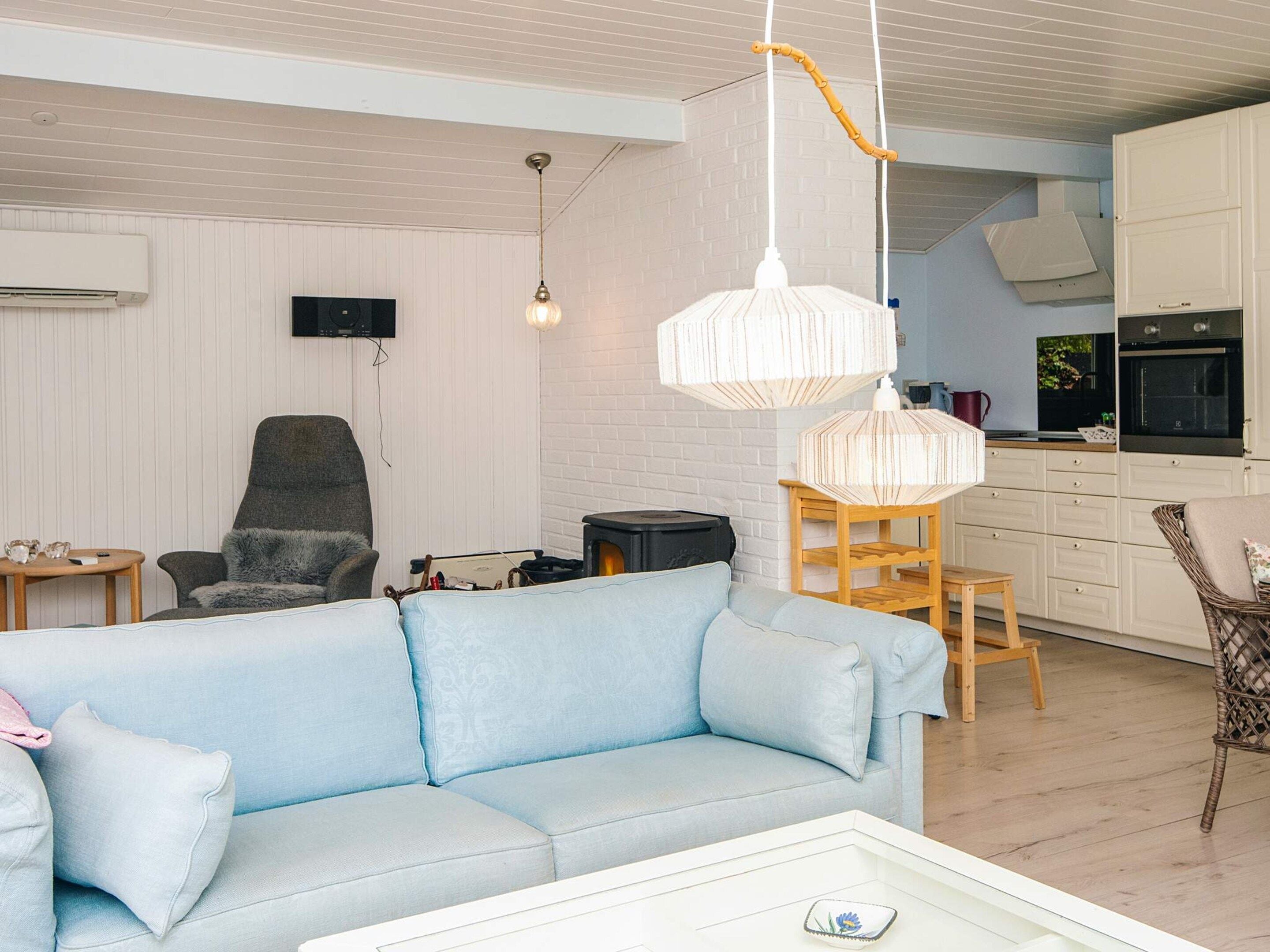 A living room with a sofa, a chair, a small table, and a kitchen area with cabinets and a stove.