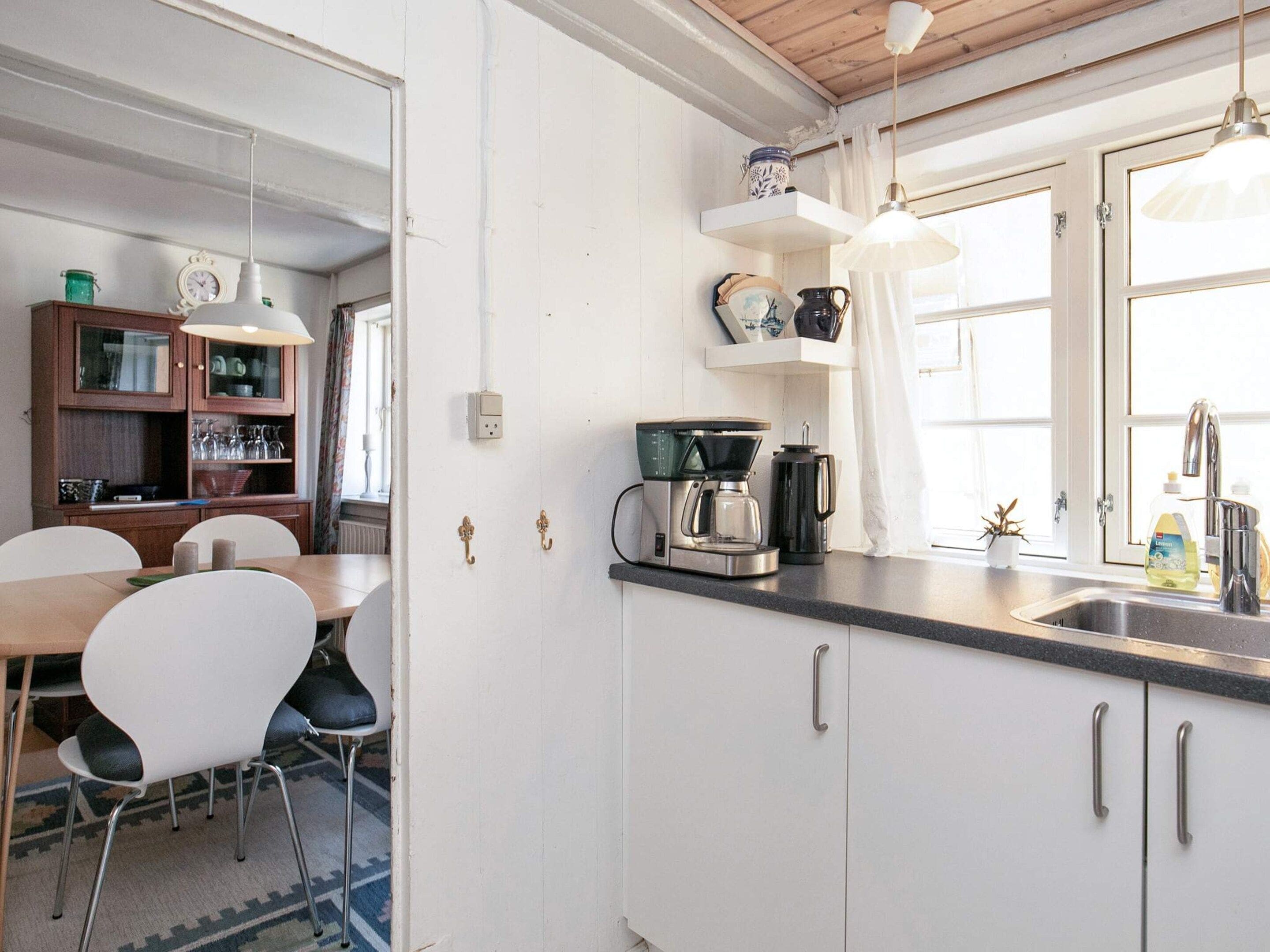 A kitchen with white cabinets, a coffee maker, and a window with curtains.