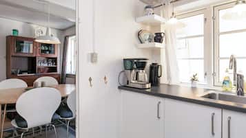 Una cocina con armarios blancos, una cafetera y un ventanal con cortinas.