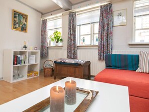 A cozy living room with a red sofa, a wooden table with candles, a bookshelf, and a window with curtains. - 3 Person Holiday Home in Aeroskobing (Aeroskobing)