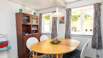 Un comedor con una mesa de madera, sillas, un armario con copas y una ventana con cortinas.