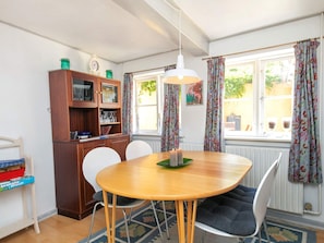 A dining area with a wooden table, chairs, a cabinet with glassware, and a window with curtains.