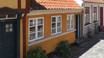 Un edificio con fachada amarilla, múltiples ventanas de marco blanco y tejado de tejas rojas.