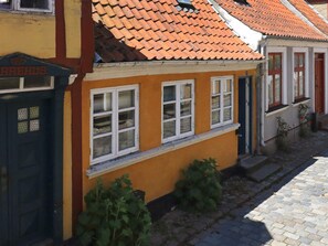 A building with a yellow facade, multiple windows with white frames, and a red-tiled roof.