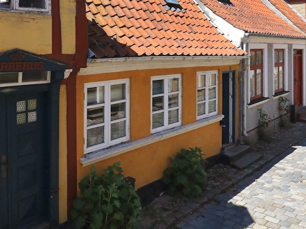 A building with a yellow facade, multiple windows with white frames, and a red-tiled roof.