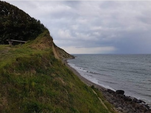 A coastal landscape with a grassy cliff and a rocky shoreline. - 3 Person Holiday Home in Aeroskobing (Aeroskobing)