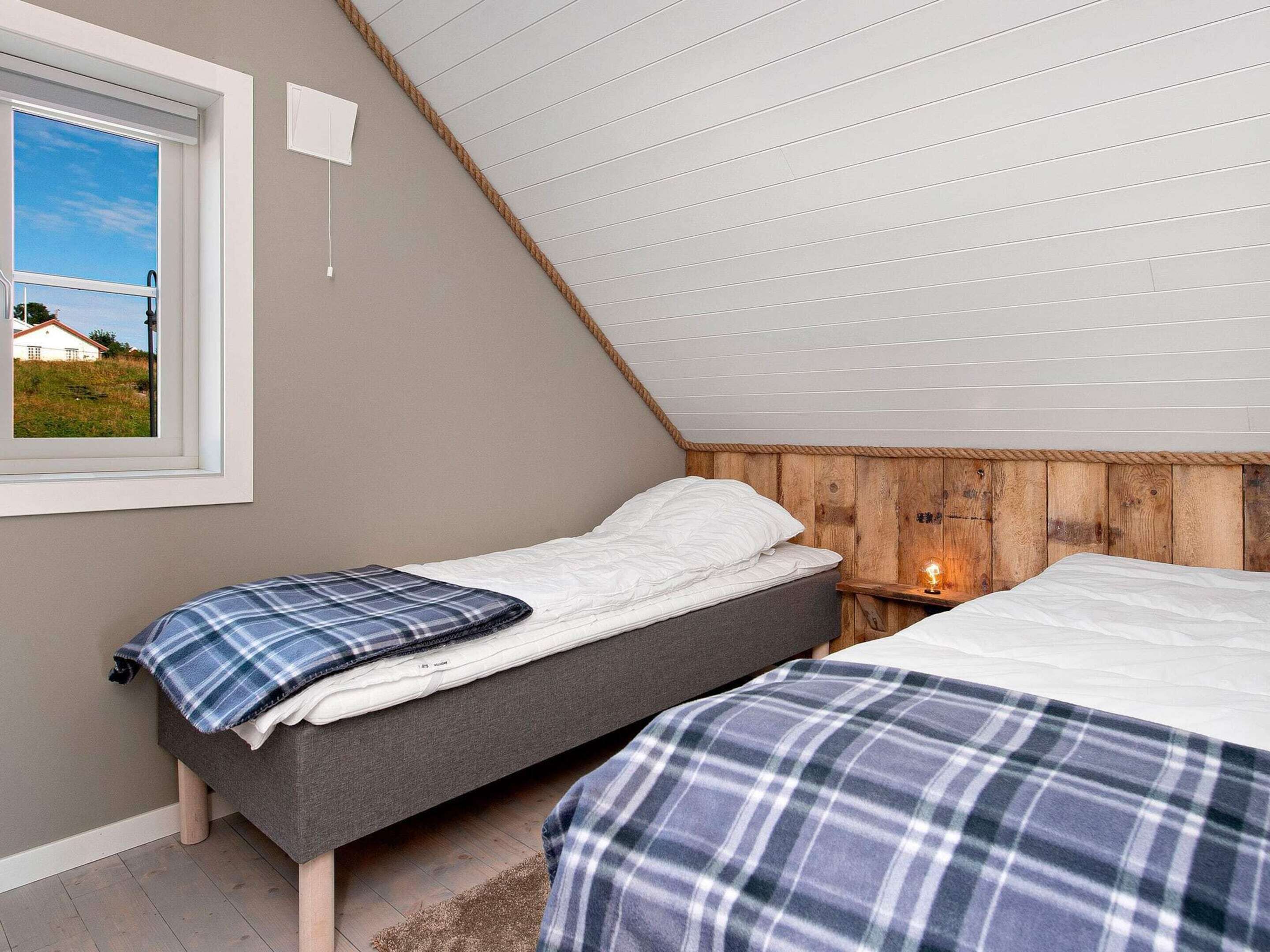 A bedroom with two beds, a window with a view, a wooden headboard, and a bedside lamp.