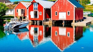 Una casa de madera roja con un bote amarrado frente a ella, ubicada junto a una masa de agua tranquila.