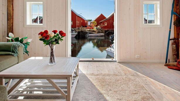 Una habitación con suelo de madera, una mesa con un jarrón de flores y vistas a edificios rojos a través de un ventanal.