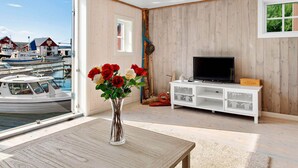 Una habitación con televisor, un armario blanco, una mesa de madera y un florero con flores.