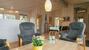 Un intérieur moderne avec des murs en bois, deux fauteuils gris, une table en bois et un vase jaune orné de fleurs.