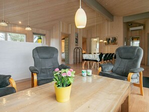 Un intérieur moderne avec des murs en bois, deux fauteuils gris, une table en bois et un vase jaune orné de fleurs.