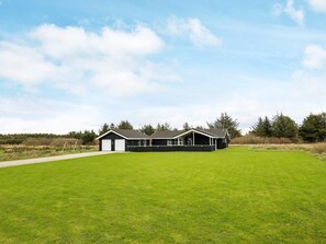 A two-story building with a flat roof, a covered driveway, and a large grassy field in front. - Holiday Home in LÃ¸kken (Lokken)