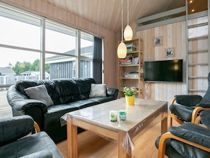 A modern living room with a leather sofa, a wooden coffee table, and a bookshelf with books and a television.