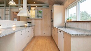 Une cuisine moderne avec des meubles en bois, des plans de travail en granit, des luminaires suspendus et une grande fenêtre.