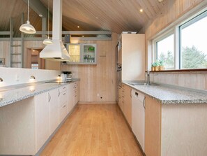 A modern kitchen with wooden cabinetry, granite countertops, pendant lighting, and a large window.