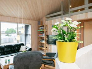A modern living room with a yellow potted plant, a black sofa, and a wooden bookshelf. - Holiday Home in LÃ¸kken (Lokken)