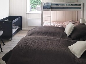 En våningssäng med en stege, ett skrivbord och en stol i ett rum med ett fönster.