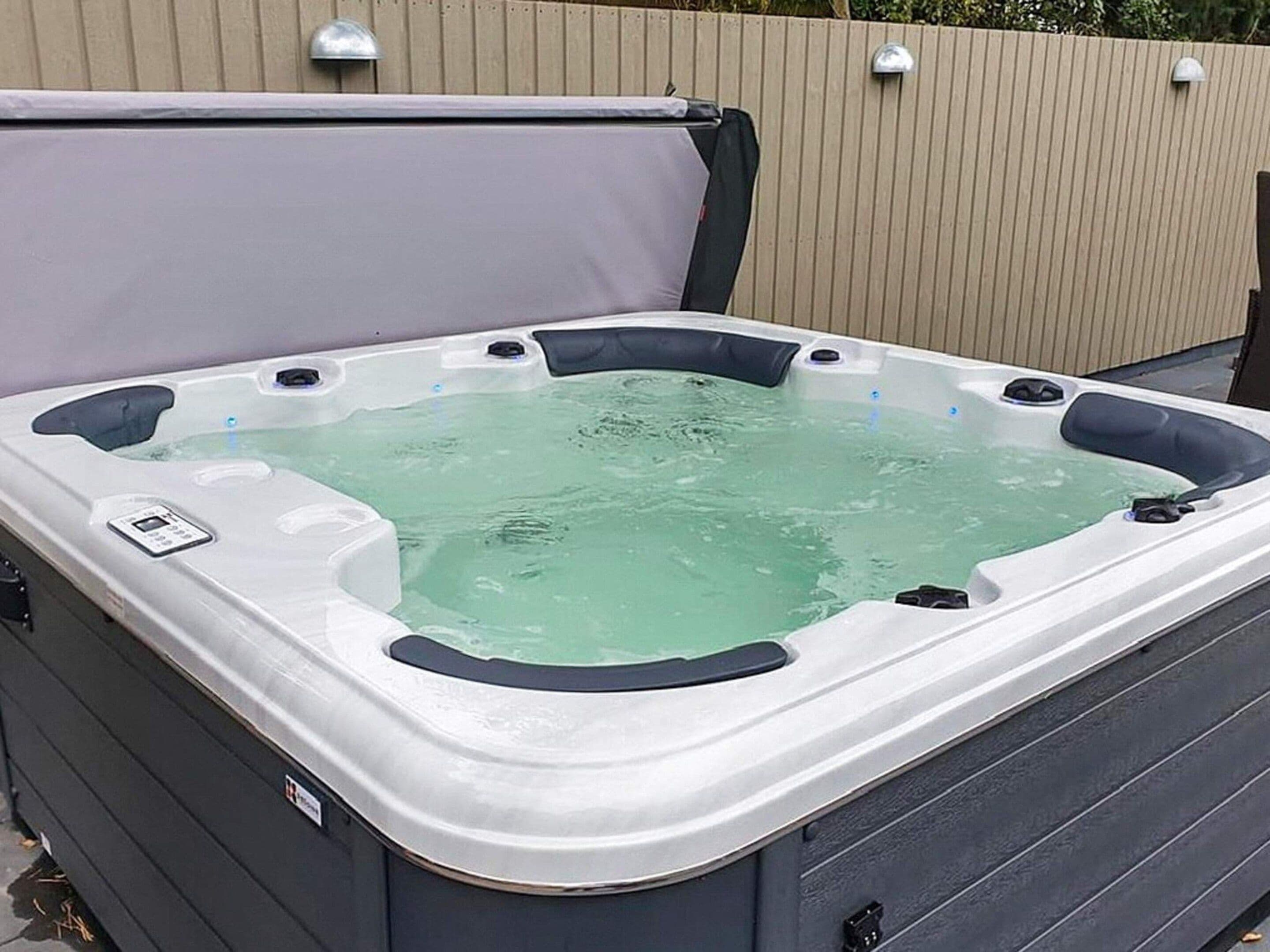 A hot tub with a control panel, surrounded by a wooden fence.