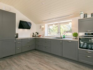 A modern kitchen with grey cabinets, a built-in oven, a window with natural light, and a flat-screen TV mounted above the counter. - Holiday Home in VÃ¦ggerlÃ¸se (Vaeggerlose)