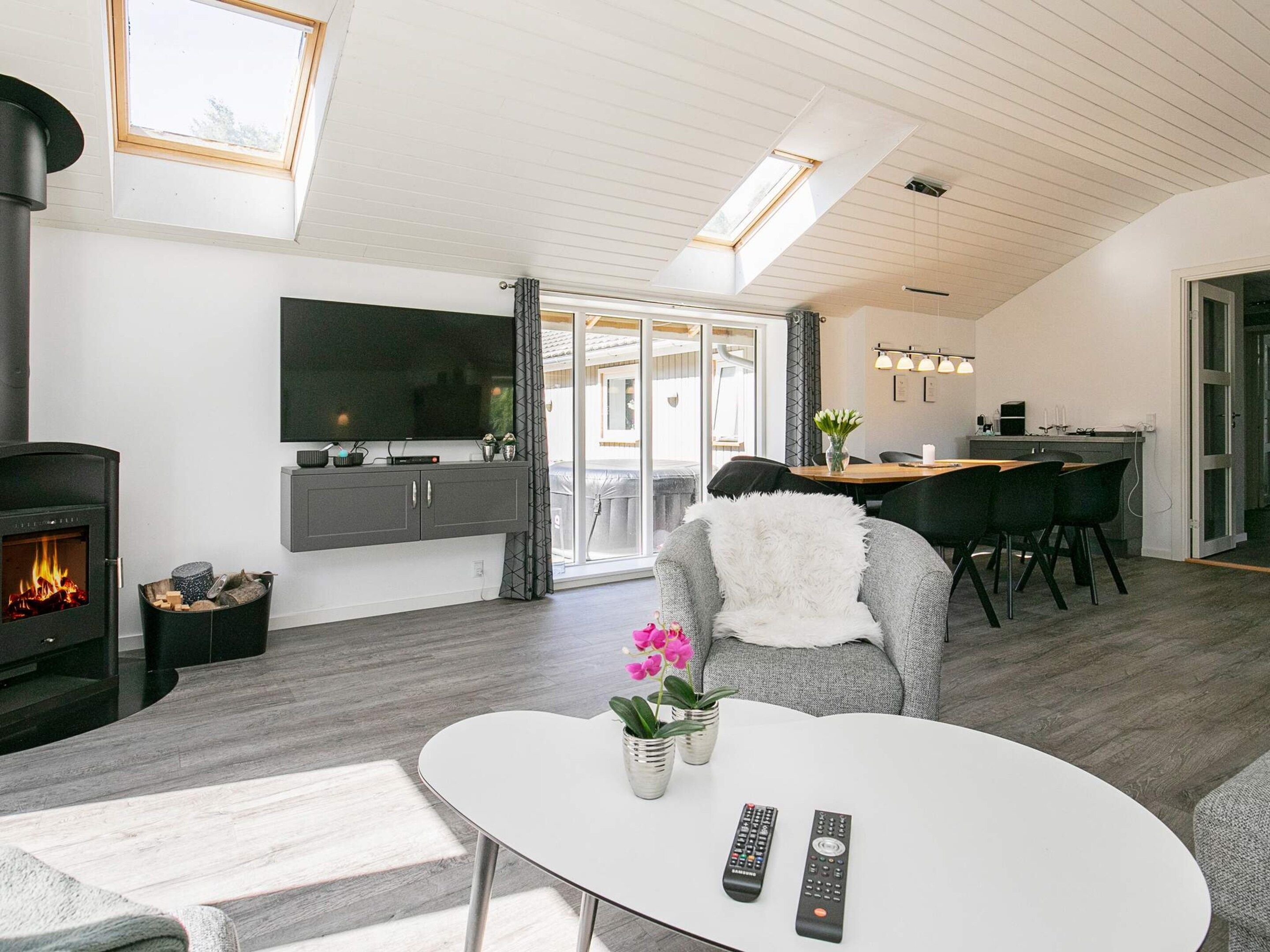 A modern living room with a fireplace, a flat-screen TV, a dining area with a table and chairs, and a kitchen visible through an open door.