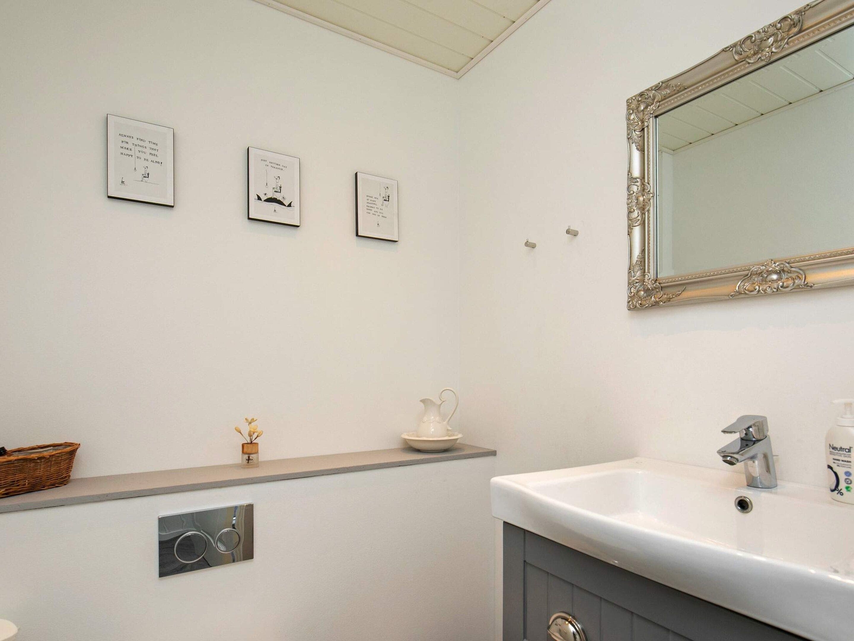 Een badkamer met een wit wastafelmeubel, een spiegel met een sierlijk frame, en drie wanddecoraties in lijsten.