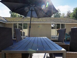 An outdoor patio with a table and chairs, a large umbrella, and a building with a tiled roof in the background.
