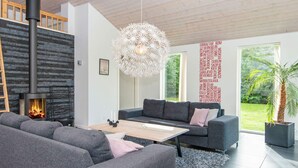 A modern living room with a fireplace, grey sofas, a coffee table, and a large window with a view of greenery.