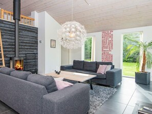 A modern living room with a fireplace, grey sofas, a coffee table, and a large window with a view of greenery.