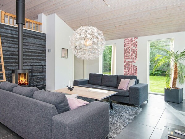 Un salon moderne avec une cheminée, des canapés gris, une table basse et une grande fenêtre donnant sur un paysage verdoyant.