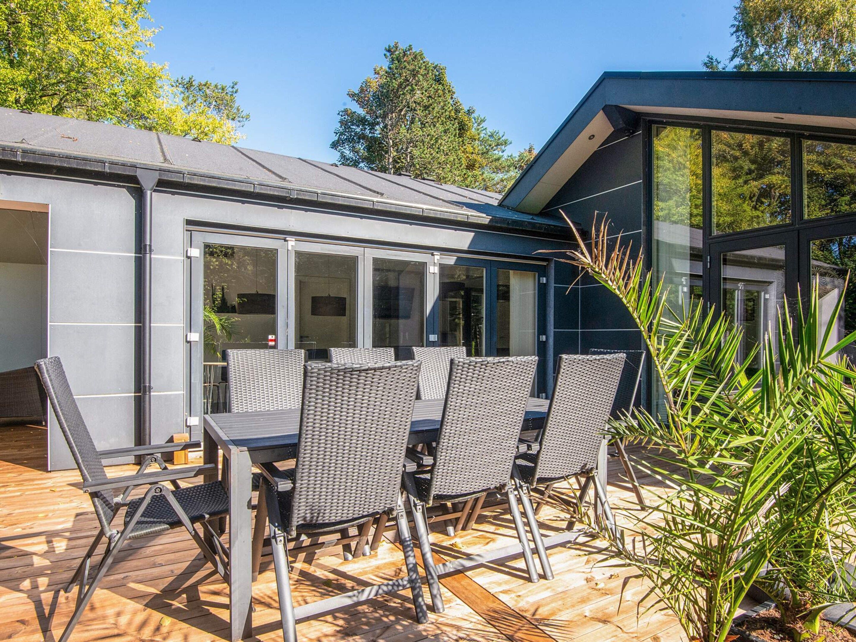 A modern outdoor dining area with a table and chairs, a wooden deck, and a glass-enclosed space.