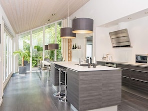A modern kitchen with a large island, bar stools, and pendant lighting. - Holiday Home in Ebeltoft (Ebeltoft)