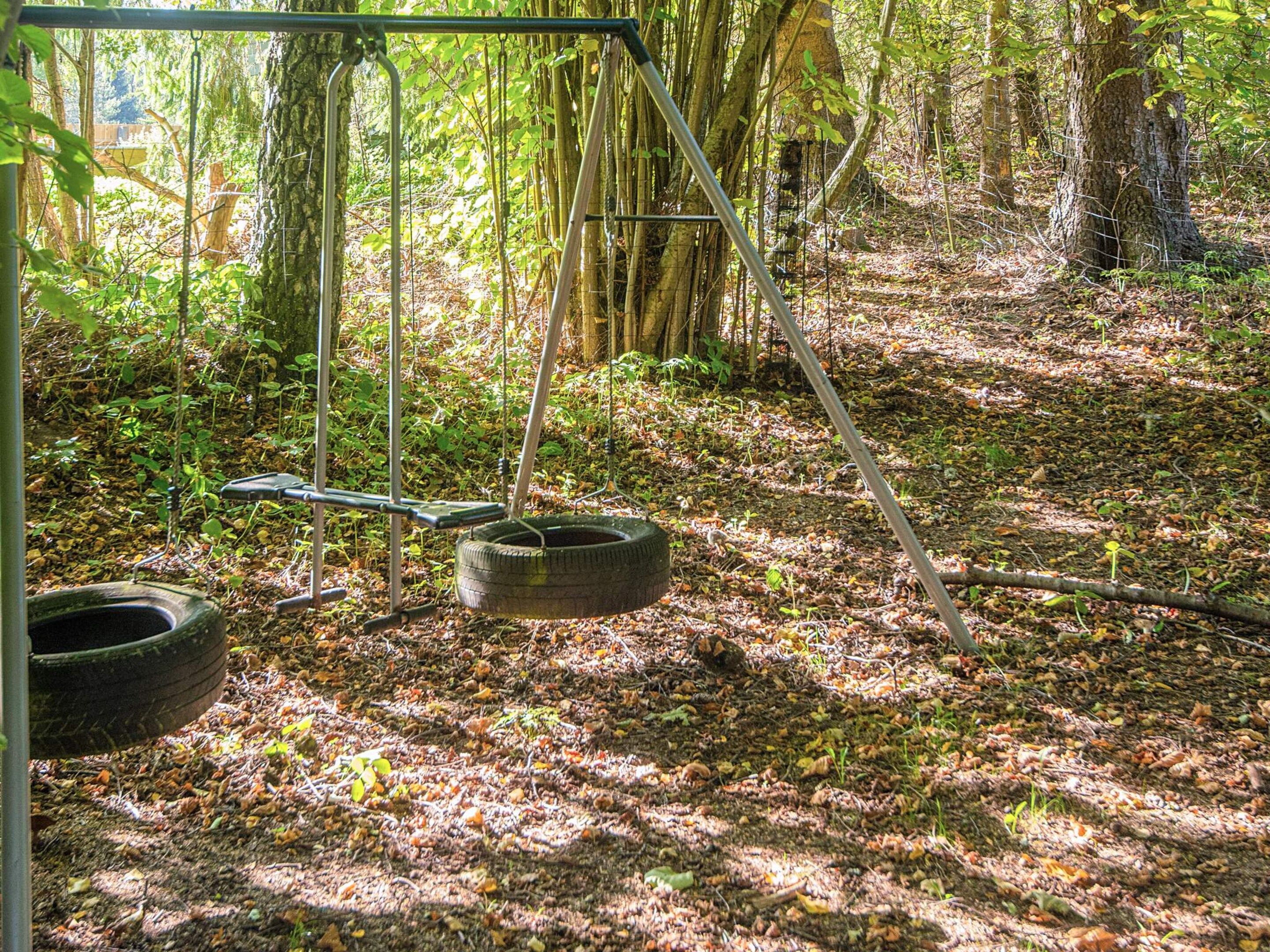 A swing set in a forested area with a tire swing hanging from a metal frame.