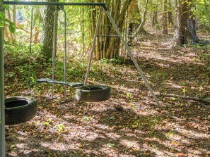 A swing set in a forested area with a tire swing hanging from a metal frame.