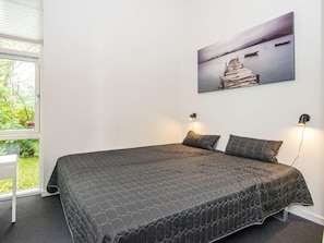 A bedroom with a bed, two bedside lamps, a window with a view of greenery, and a wall-mounted painting. - Holiday Home in Ebeltoft (Ebeltoft)