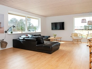 A modern living room with a black leather sofa, a wooden coffee table, wicker chairs, and large windows with a view of trees and buildings.