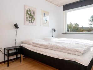 A bedroom with a bed, two wall-mounted lamps, and two framed botanical illustrations.