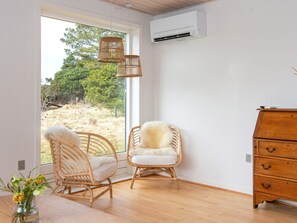 A room with wicker chairs, a wooden dresser, and an air conditioning unit.