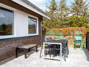 A patio with a table and chairs, a bench, and a view of a brick wall with a window.