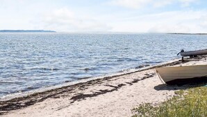 A beach with a boat on the sand and calm water. - Cozy Coastal Cottage at Jegindo-by Traum (Thyholm)