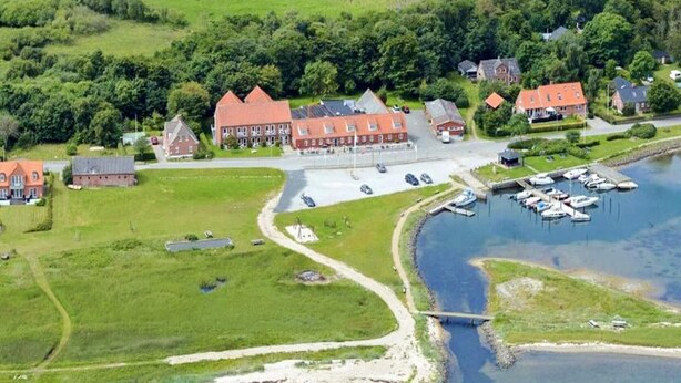 An aerial view of a lakeside property with multiple buildings, a marina, and a bridge connecting the land to the water. - Cozy Coastal Cottage at Jegindo-by Traum (Thyholm)