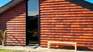 Un edificio moderno con techo inclinado, un amplio ventanal y un banco de madera en el exterior.