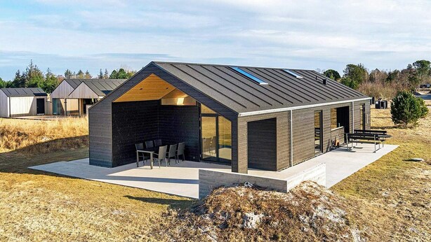 Una casa moderna con techo inclinado, un porche cubierto con mobiliario y vistas del paisaje circundante.