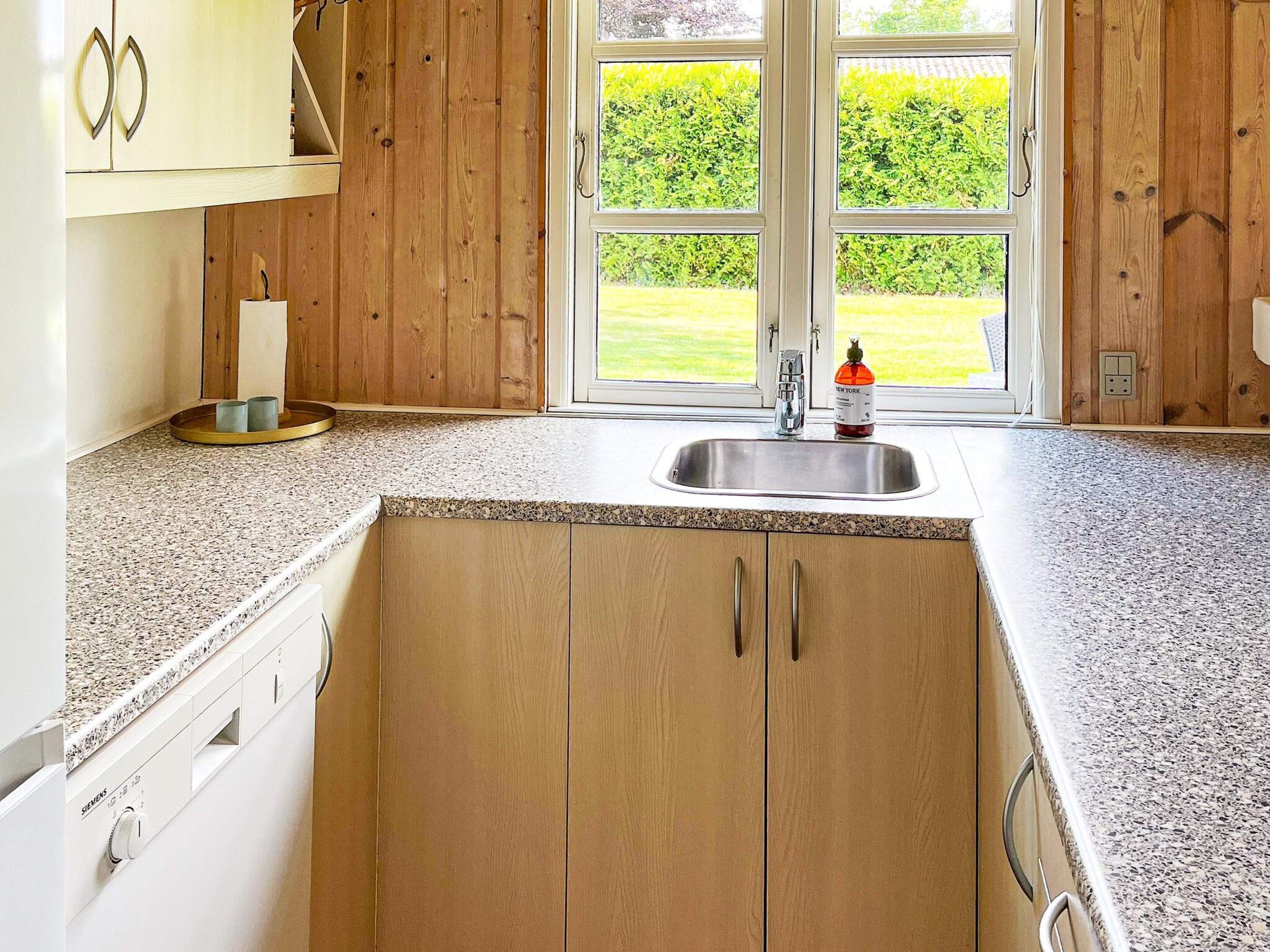 A kitchen with wooden cabinets, a granite countertop, a stainless steel sink, and a window with a view of a green lawn.