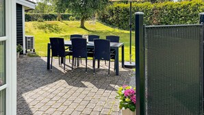 An outdoor patio with a table and chairs, an umbrella, and a view of a green landscape. - Holiday Home in Hadsund (Hadsund)