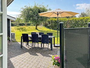 An outdoor patio with a table and chairs, an umbrella, and a view of a green landscape. - Holiday Home in Hadsund (Hadsund)