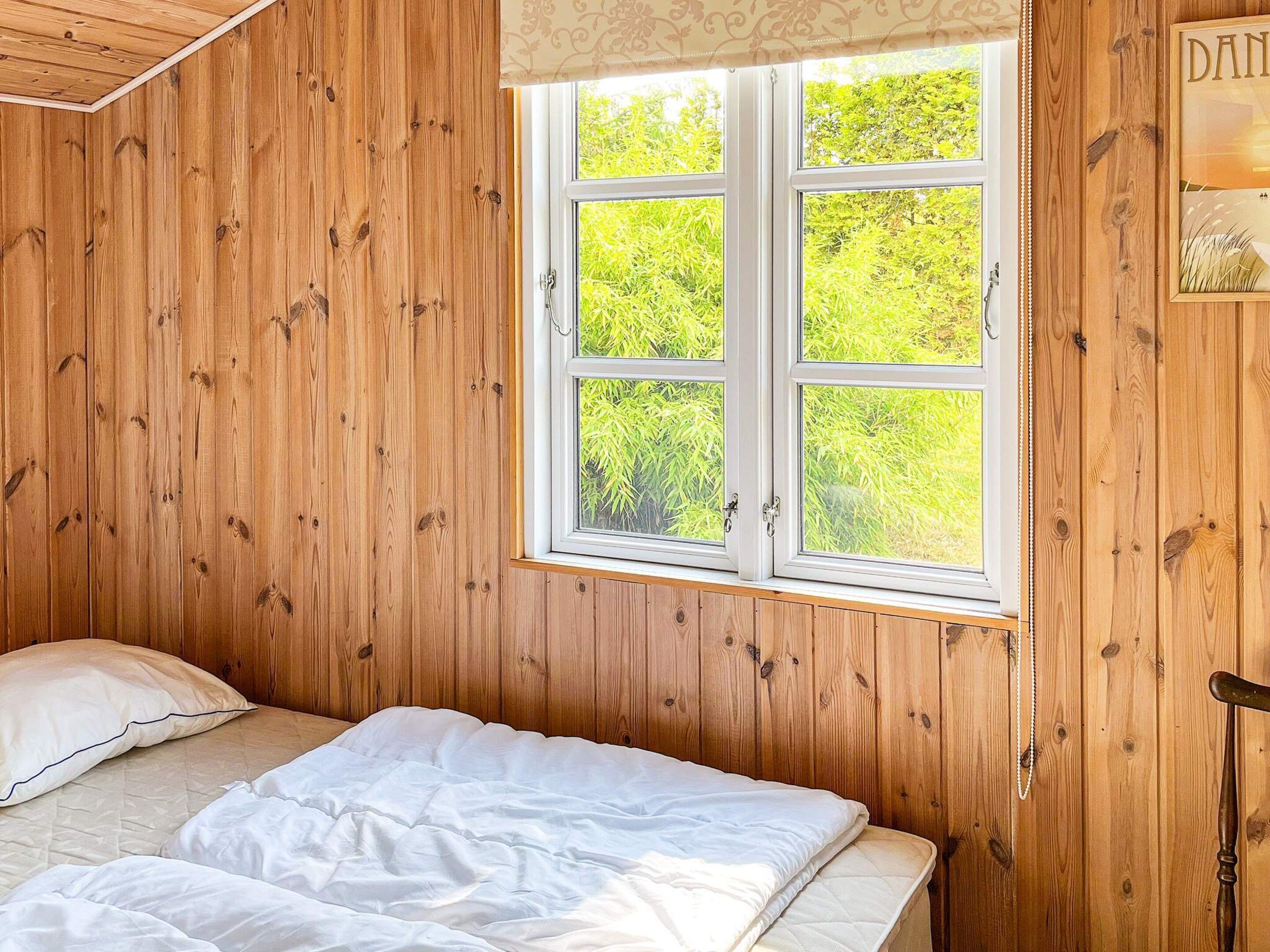 A wooden-paneled room with a bed, a window, and a door.